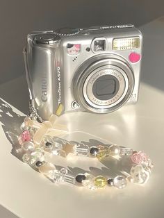 a silver camera sitting on top of a table next to a chain with beads and charms