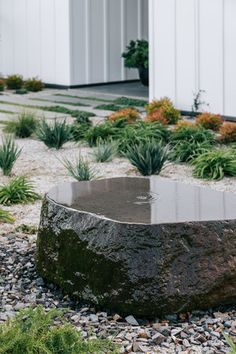 a large rock sitting in the middle of a gravel field next to a white building