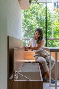 a woman sitting on the edge of a sink in front of a window with trees outside