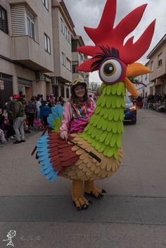 a woman is dressed up as a rooster in the middle of a street with people watching