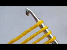 two knitting needles are hooked up to the ends of yellow yarn and metal hooks on a gray background