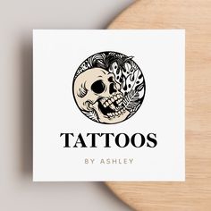 the logo for tattoos by ashley features a skull and floral designs on white paper