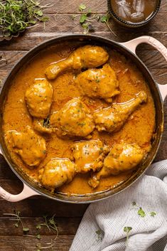 a pan filled with chicken and sauce on top of a wooden table