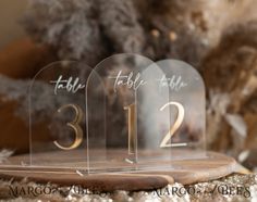 three clear acrylic table numbers sitting on top of a wooden board