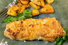 fish, potatoes and greens on a green plate with a fork next to the dish