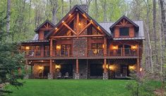 a large log home in the woods with lights on it's porch and windows