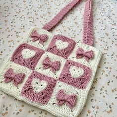 a pink and white crocheted bag with hearts on it sitting on a bed