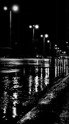 black and white photograph of street lights reflecting in the water at night with reflections on wet pavement