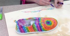 a person painting a pair of shoes with crochet on the table next to some markers