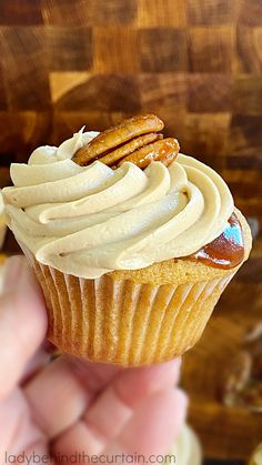 a hand holding a cupcake with frosting and pretzels on top