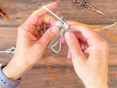 two hands are holding scissors and string on a wooden table with other crafting supplies