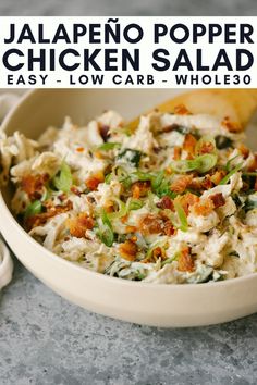 a white bowl filled with chicken salad next to a wooden spoon on top of a table