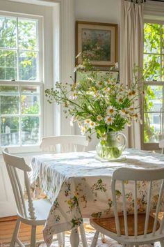 a dining room table with flowers in a vase on it and chairs around the table