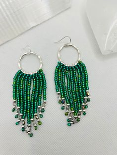 These fabulous beaded fringe earrings have a romantic boho chic vibe and are so light and easy to wear! Delicate strands of iridescent emerald green Czech glass seed beads cascade beautifully from silver coloured brass hoops. Handwoven with love by yours truly, each strand is completed with silver plated beads, Czech fire polished crystals   and a tiny hematite star charm adorns the centre strand.  The finished length of these earrings is approximately 3 inches (7.5cm) and 1.25 inches (3cm) across. The ear wires are silver plated and nickel free.  This listing is for one pair of earrings only. The video showing multiple pieces are for display purposes only. The additional earrings are also available in my shop under separate listings. These earrings would make a wonderful gift for someone Green Fringe Jewelry For Festivals, Green Fringe Jewelry For Festival, Handmade Green Tassel Earrings For Party, Nickel-free Green Beaded Earrings For Parties, Bohemian Green Beaded Hoop Earrings, Adjustable Green Chandelier Earrings With Dangling Beads, Adjustable Green Jewelry With Tassels, Bohemian Green Chandelier Earrings For Festival, Bohemian Dangle Fringe Hoop Earrings