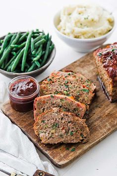 slices of meatloaf on a cutting board with green beans and mashed potatoes