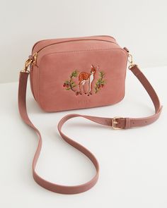 One bag, endless adventures. A timeless, structured camera bag with a spacious compartment and zipped inside pocket, suitable to keep your treasures safe for daily activities or weekend explorations alike. This versatile piece is crafted in dusty pink, soft suede-like fabric, featuring an adorable embroidered fawn design, and finished with gold-tone hardware. Timeless Purse, Fable England, Embroidered Backpack, Fawn Design, Chic Crossbody Bag, Hand Painted Jewelry, Animal Brooch, Across Body Bag, Pink Suede