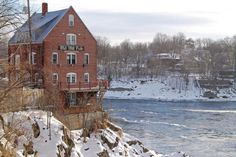 a red brick building sitting on top of a snow covered hillside next to a river