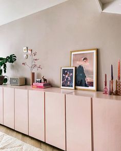 a living room with pink cabinets and pictures on the wall next to plants in vases