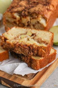 two slices of apple bread on a cutting board with apples in the background and one slice cut off