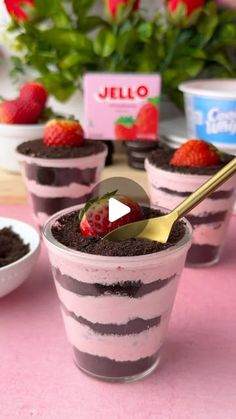 desserts with strawberries and chocolate in small cups on a pink tableclothed surface