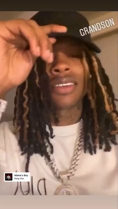 a man with dreadlocks wearing a baseball cap and looking at the camera while holding his hand up to his face