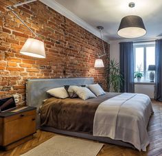 a bedroom with brick walls and wooden floors is pictured in this image, the bed has two lamps on either side of it