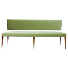 a green bench sitting on top of a white floor next to a wooden leg chair