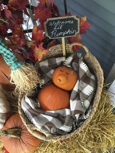 a basket filled with pumpkins sitting on top of hay next to a welcome sign