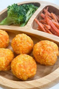 four balls of food on a wooden plate with carrots and broccoli in the background