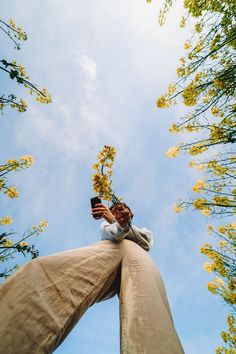 a person standing in the middle of tall trees holding a cell phone up to their ear