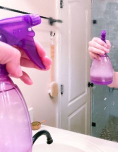 a woman is holding a purple spray bottle in front of a bathroom mirror and looking at her reflection