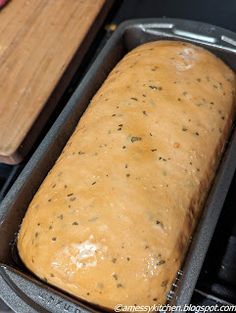 a loaf of bread sitting in a pan on top of a counter next to a cutting board