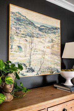 a painting is hanging on the wall above a dresser with a lamp and potted plant