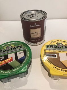 three tins of paint sitting next to each other on a white counter top in front of a wall