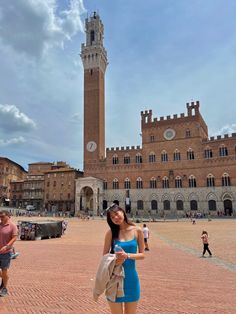 a woman standing in front of a tall building with a clock on it's tower