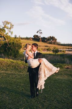 a man carrying a woman in his arms while standing on top of a lush green field