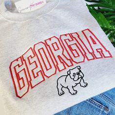 "Experience the perfect blend of style and school spirit with our Georgia Bulldog Crewneck Sweatshirt or T-shirt! Available in three colors, this sweatshirt is designed to keep you cozy and comfortable, whether you're cheering in the stands or just showing off your Bulldog pride around town. At the heart of its design is the iconic \"Georgia\" embroidery, boldly presented across the center chest. The word is intricately stitched in a vibrant red, capturing the essence of the University of Georgi Georgia Bulldogs Shirts Vinyl Men, College Sweatshirt With Letter Embroidery For School Spirit, College Sweatshirt With Letter Embroidery, Sporty Letter Embroidery Sweatshirt For School, Collegiate Sweatshirt With Embroidered Graphics, Varsity Sweatshirt With Letter Embroidery For College, College School Spirit Sweatshirt With Embroidered Logo, Varsity Sweatshirt With Letter Embroidery For School, Collegiate Letter Embroidery Sweatshirt For College