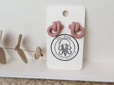 a pair of pink ear clips sitting on top of a white card next to a plant