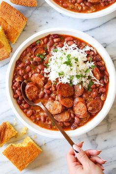 two white bowls filled with chili and beans next to toast on a marble counter top