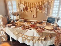 a table topped with pizzas and pies next to a baby shower sign that reads welcome baby