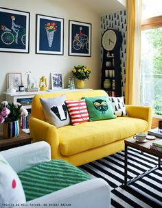 a living room with yellow couches and pictures on the wall above them, along with other furniture