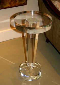 a clear glass table with a circular base on the floor in front of a couch