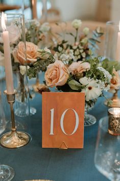 an orange table number sitting on top of a blue table cloth with flowers and candles