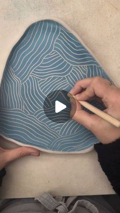 two hands holding chopsticks over a blue plate with wavy designs on the surface