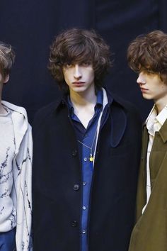 three young men standing next to each other in front of a black background wearing coats