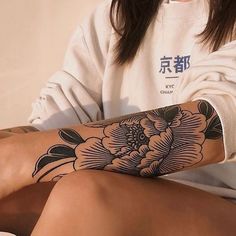 a woman with a flower tattoo on her arm and leg is sitting in front of a white wall