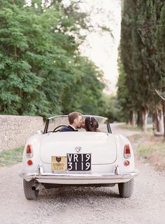 a bride and groom kissing in the back of an old car on a country road