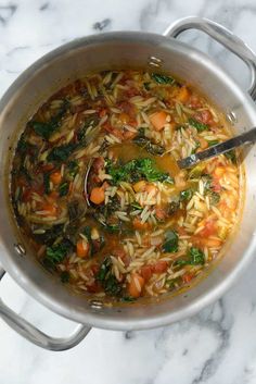 a pot filled with pasta and vegetables on top of a marble countertop next to a spoon