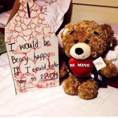 a brown teddy bear sitting on top of a bed next to a valentine's day sign