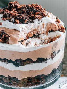 a layered cake with white frosting and chocolate crumbs on top is sitting on a glass platter